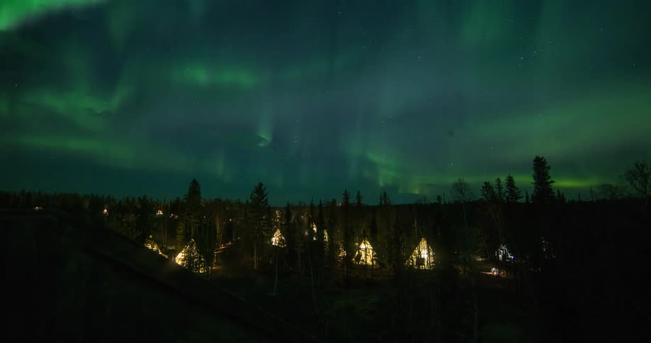 Lighted tepee tents under green northern lights
