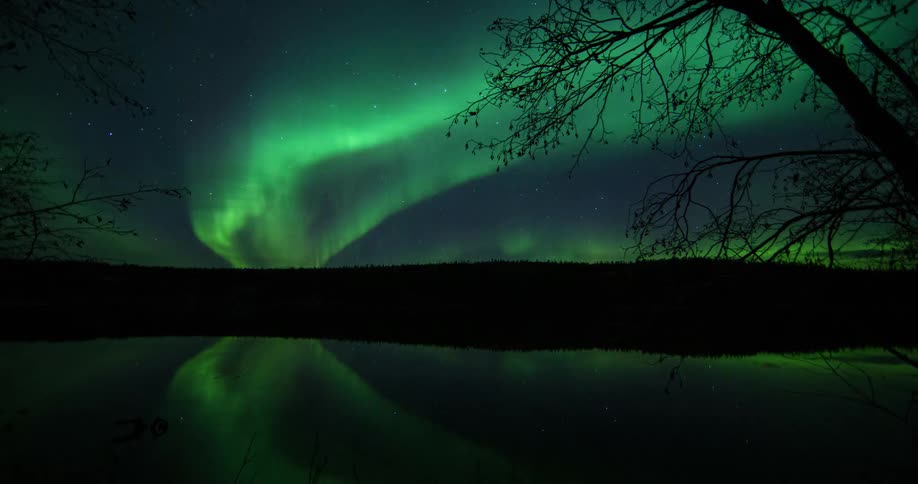 Aurora borealis moves across star filled sky and reflects onto lake