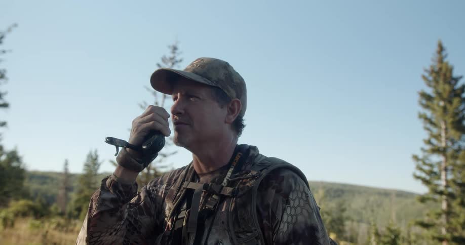 A man hunting in a forest talks on a walkie talkie