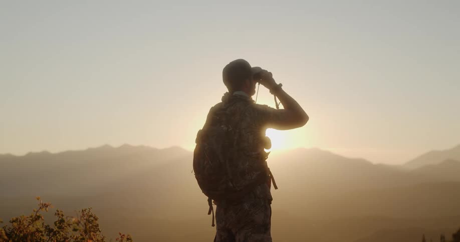 A man out hunting looks through binoculars