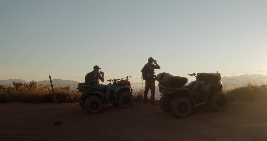 Two men next to their atvs look out at the landscape