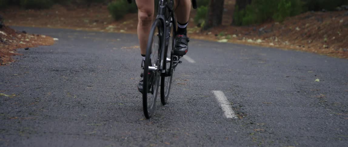 frontal medium tracking shot of cyclist pedaling up an asphalt road