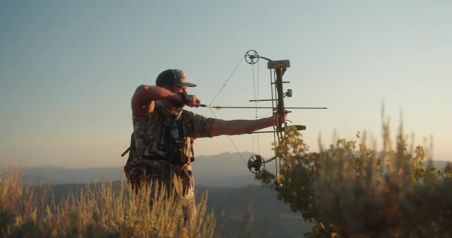 A man out hunting raises a bow in the air and aims