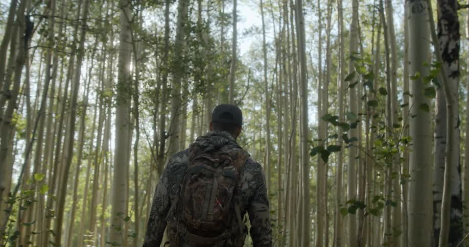 Man wearing camouflage clothes and a backpack walk into forest