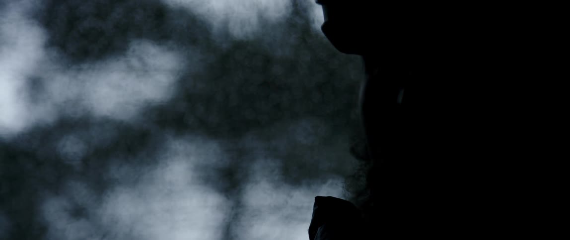 silhouette of a man looking outside through a car window covered in water drops