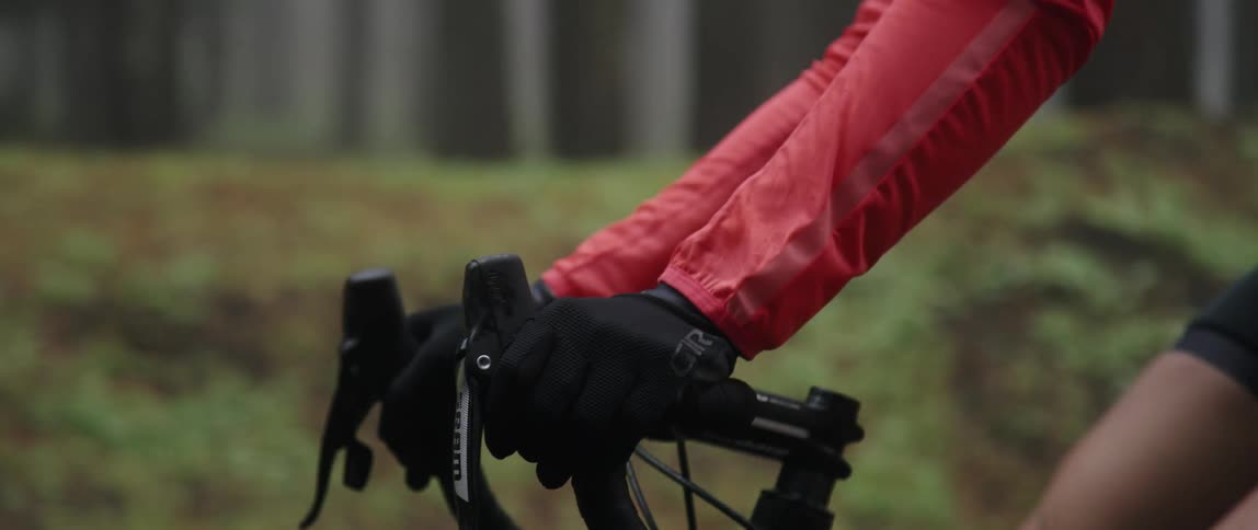 A cyclist grips the handlebars of a bicycle while riding a bicycle through a woodland