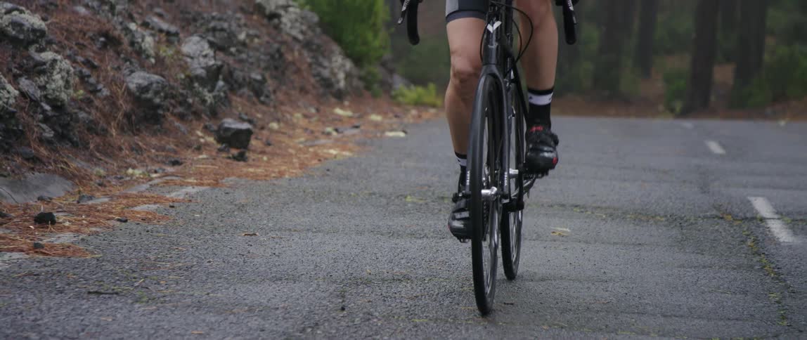 frontal medium tracking shot of cyclist pedaling on an asphalt road