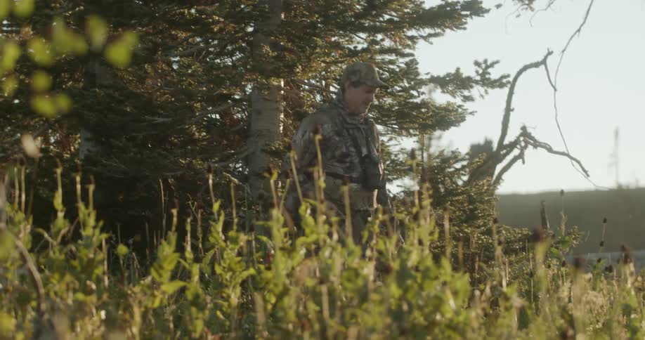 A man hunting in a forest walking with a bow and arrow