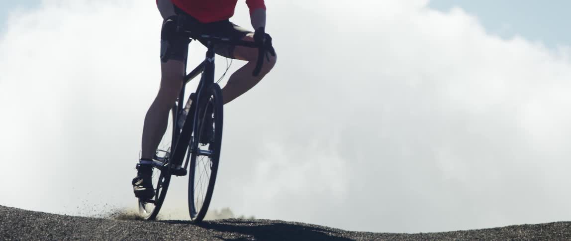 cyclist going over a hill with a breaking maneuver with clouds and horizon in the background