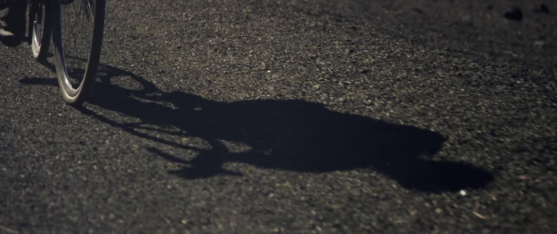 the shadow of a bicyclist pedaling on black gravel