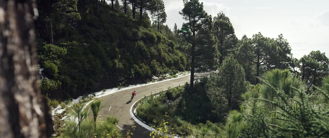 super wide shot of a Cyclist riding downhill through a curve on a scenic mountain forest road