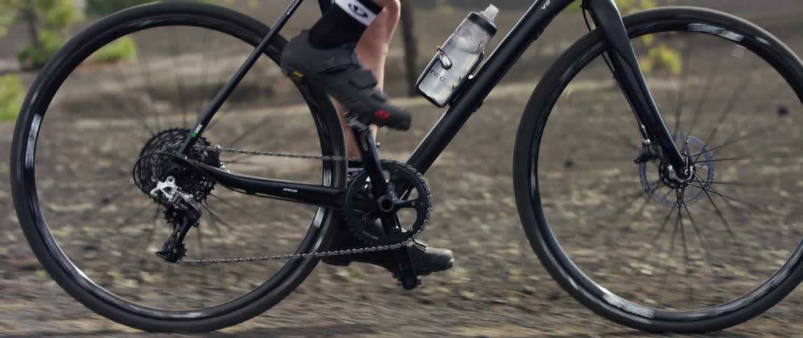side tracking shot of a gravel bike riding over black dirt gravel