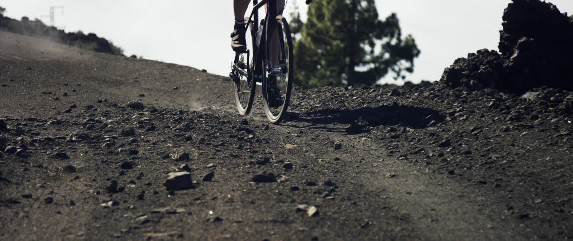 Cyclist breaking and steering into a curve on a black gravel dirt road