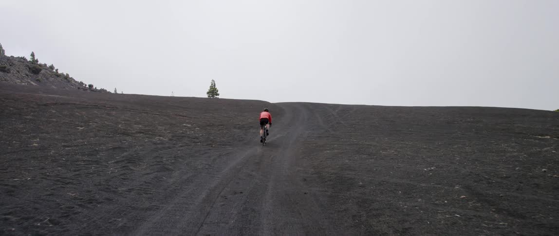Cyclist rides bicycle on open dirt road in black volcanic landscape
