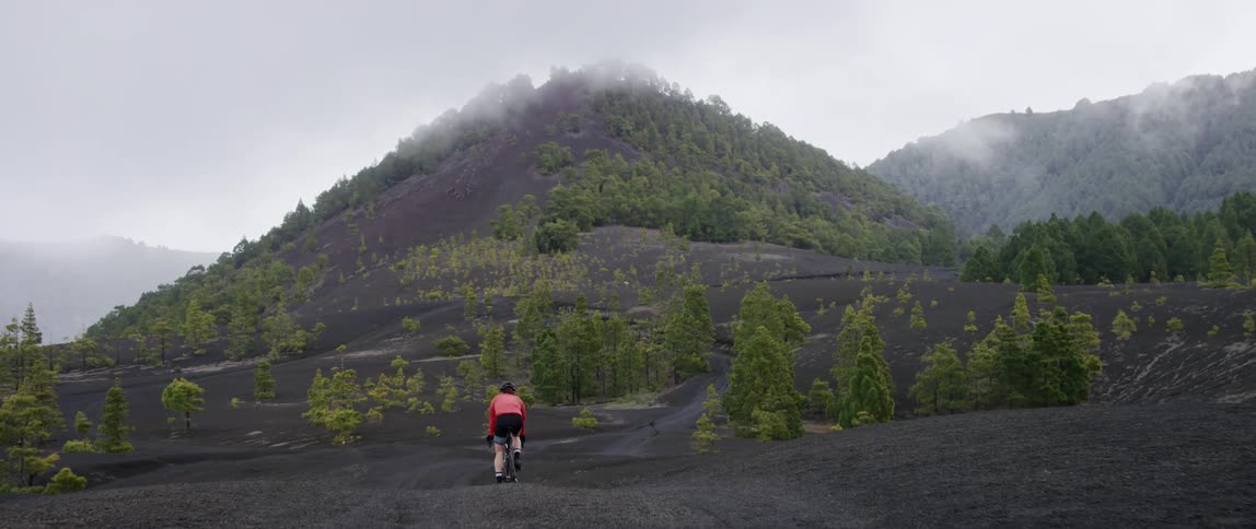 bicyclist going over a hill revealing a black volcanic landscape