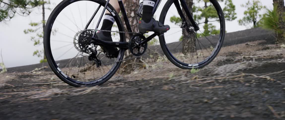 cyclist pedaling his bicycle uphill through a forest over black gravel