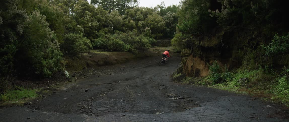 wide shot of a cyclist going downhill around a corner on a dirtroad