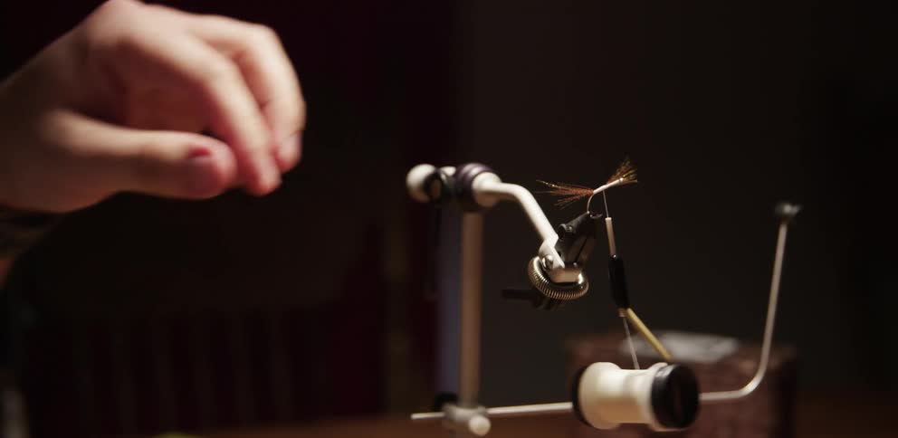A person is making a fishing lure with wire and line indoors