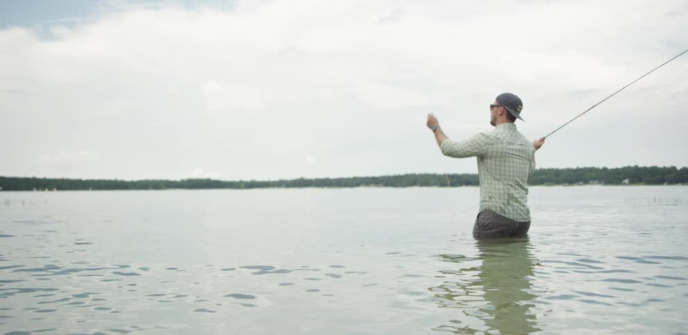 Fisherman standing in a large lake fly fishing on a cloudy day