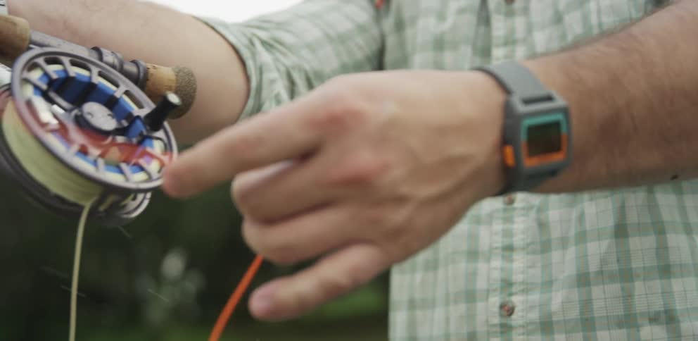 A man adjusts his fishing rod to cast out a line while standing outside