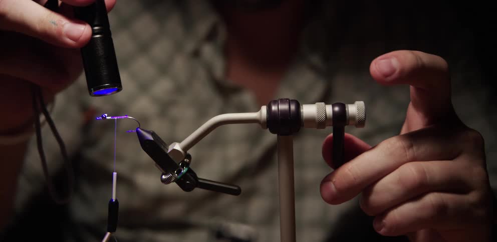A man crafting a fishing hook cures resin with an uv light lamp
