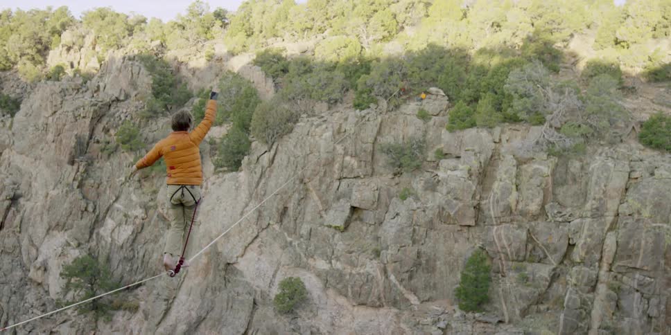 Person walking a high wire across a deep canyon wearing a safety belt