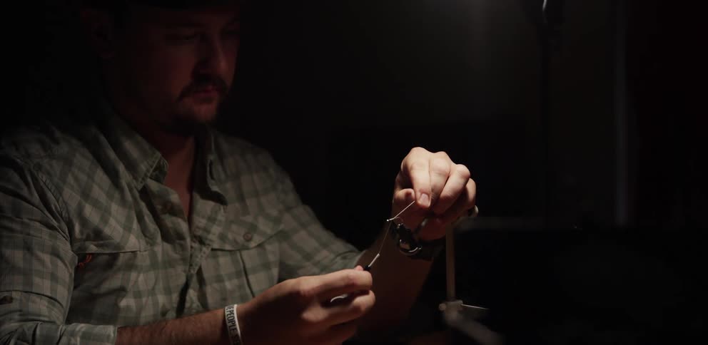A man sitting in a room tying a fly for fly fishing