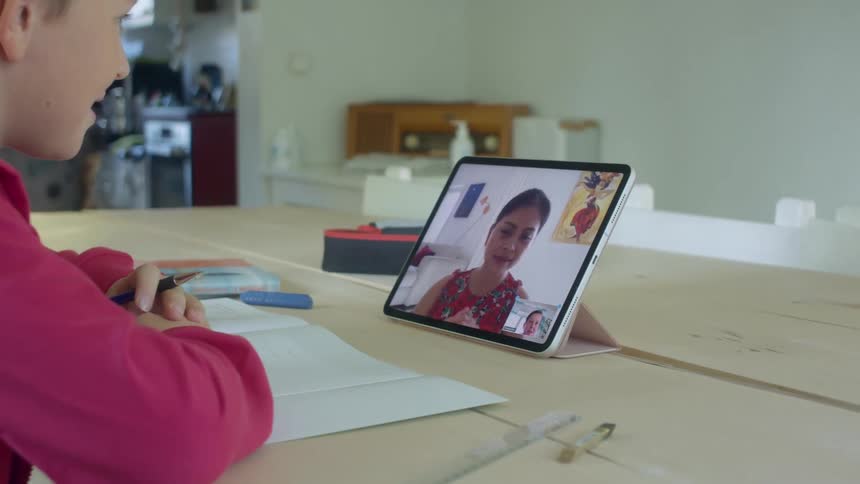 A child at home listens to his teacher on a tablet and does school work