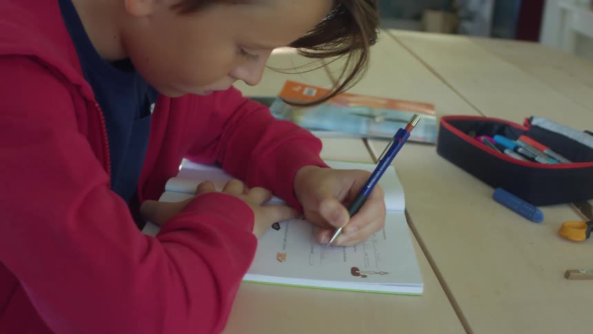 A boy sits at a table writing in a book