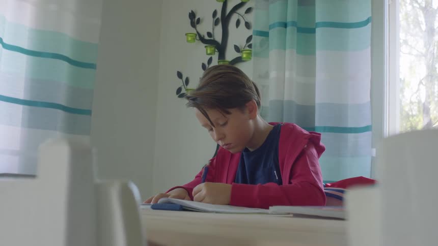 Boy with a red zip up hoodie sits and studies at the desk in a room