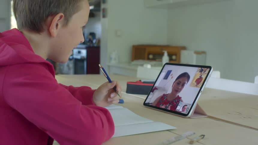 A young boy at home interacts with his teacher on a tablet and does school work