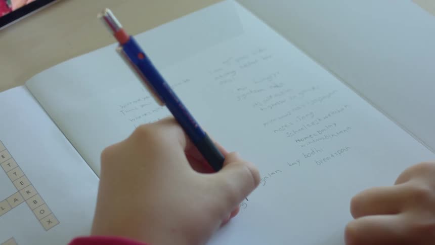 A boy does schoolwork at home in front of a tablet