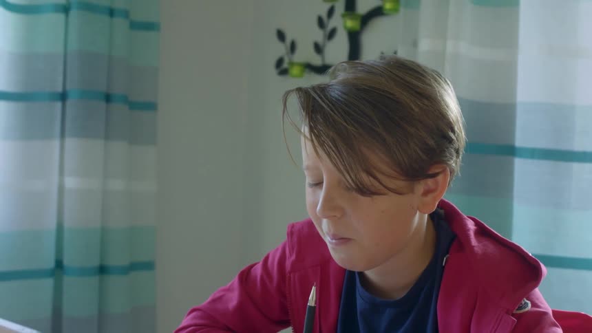Young boy completing school work sitting in front of a tablet at a dining room table