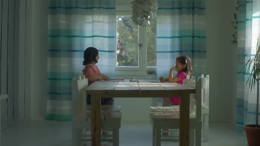 Two girls doing homework over the dinner table in a room at home