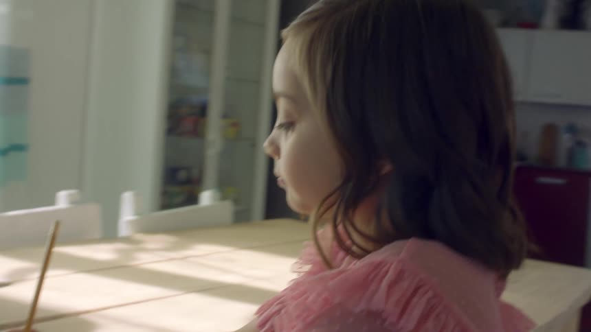 Two young girls sit at a home table with a tablet having a video call and doing school work