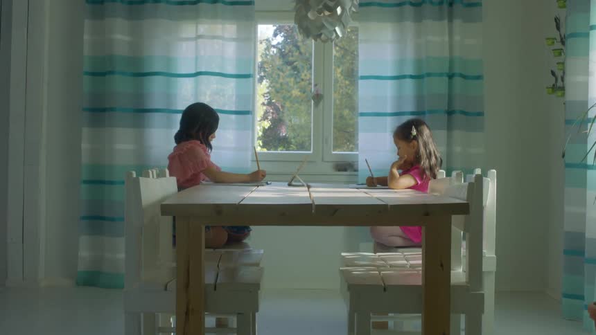 Two young girls sit at their kitchen table doing homework