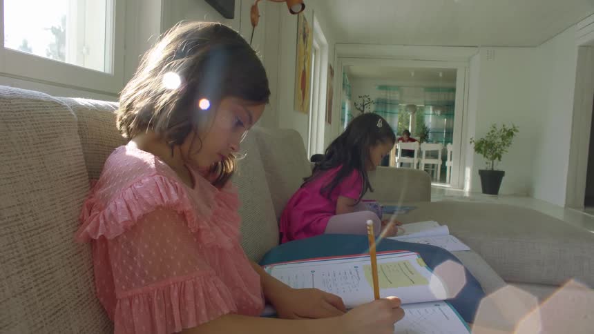 Two girls sitting on a beige sofa do homework in the living room at home