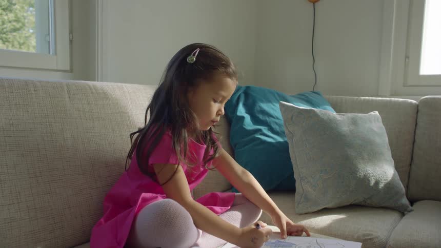 A little girl sits on a couch at home and colors
