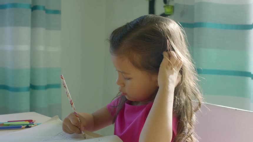 A young girl sits at a table at home and draws in a book