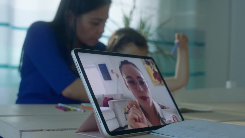 Mother and daughter doing homework on a video call through a tablet