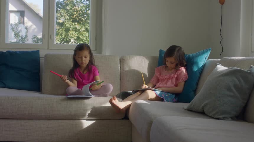 Two young girls sit on a couch writing in books