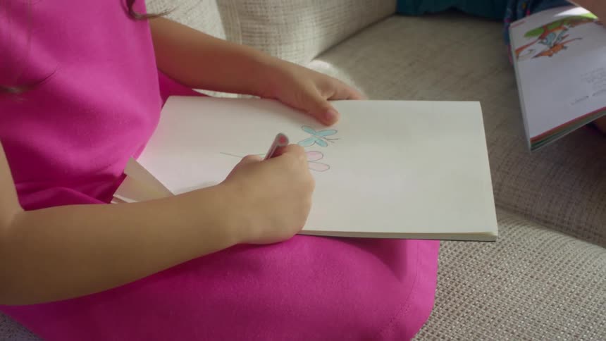 A girl in a room sitting on a couch drawing on a scrapbook