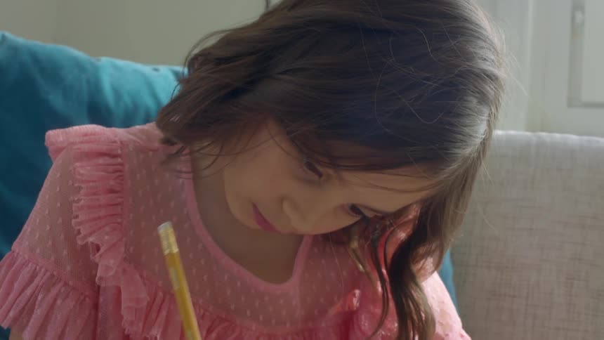 Girl with a pink blouse sits on the beige sofa and writes in a notebook