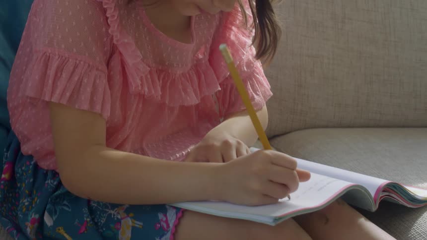 A little girl at home sits on a couch and does school work