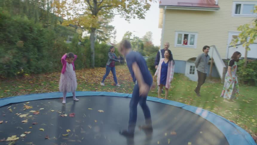 A boy and two girls jumping and doing back flips over a trampoline in the backyard