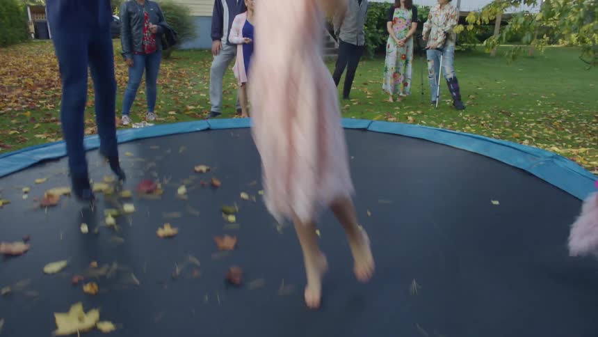 Group of children having fun jumping on a trampoline in the backyard next to their parents