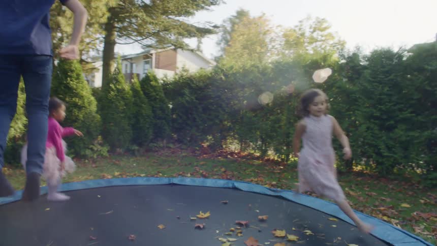 A boy and two girls jumping over a trampoline in the backyard at home