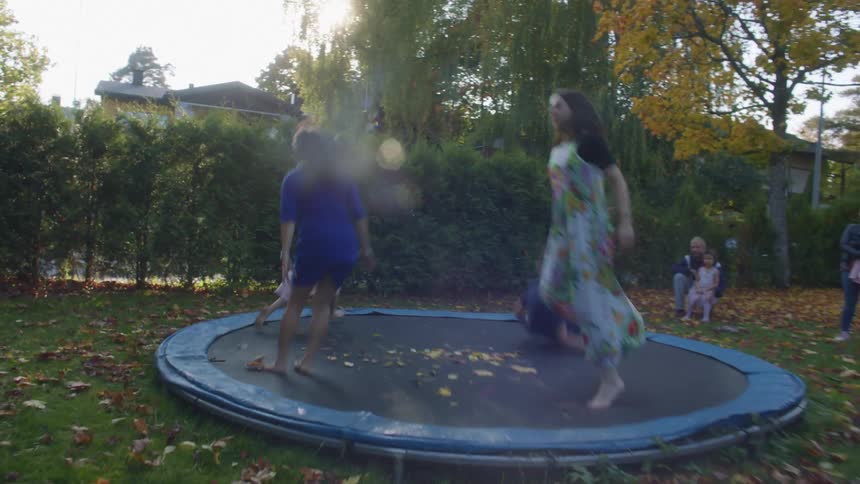 As others watch in the backyard kids jump on a trampoline at dusk