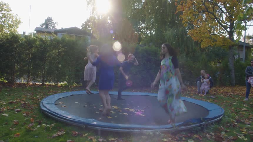 Family and friends in a party jumping on a trampoline in the backyard at home