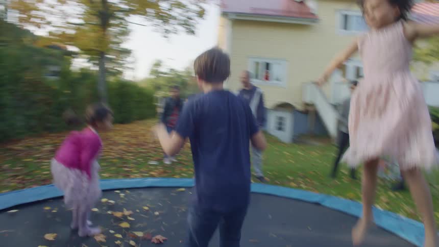 A group of children jump on a trampoline in a backyard